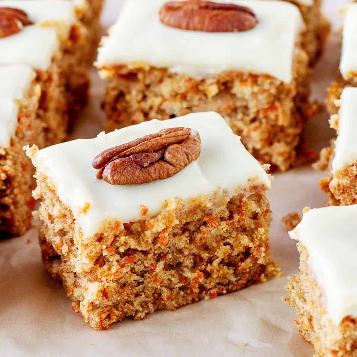 Squares of carrot cake with frosting and pecan, on white paper