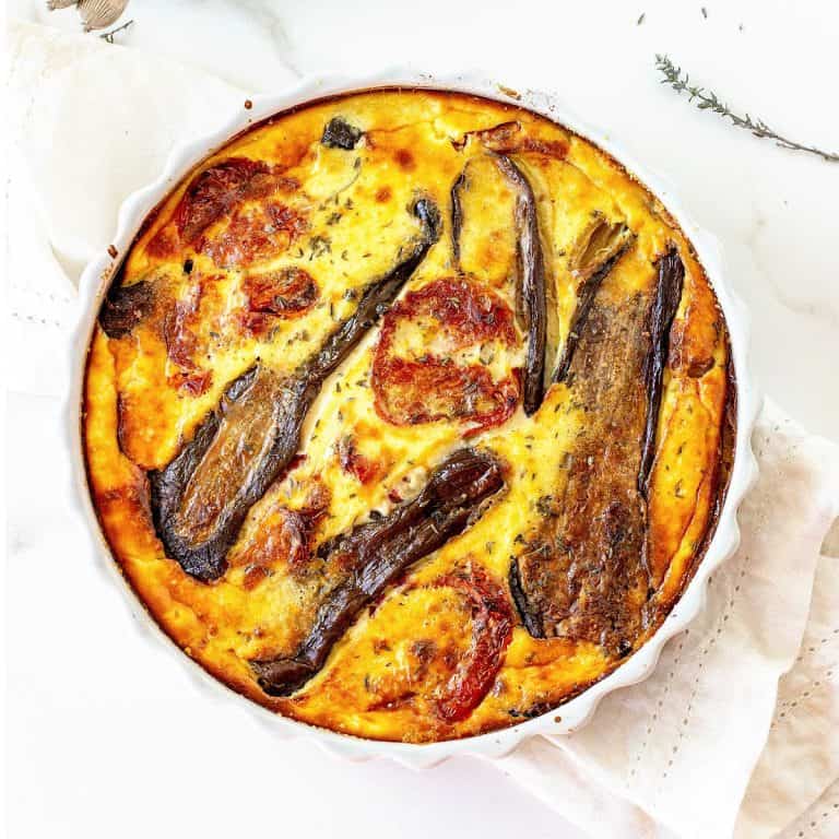 Round dish with baked quiche on white surface