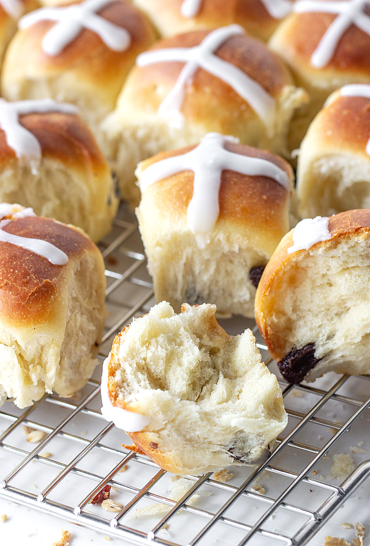 One half and whole small buns with white cross on top on wire rack