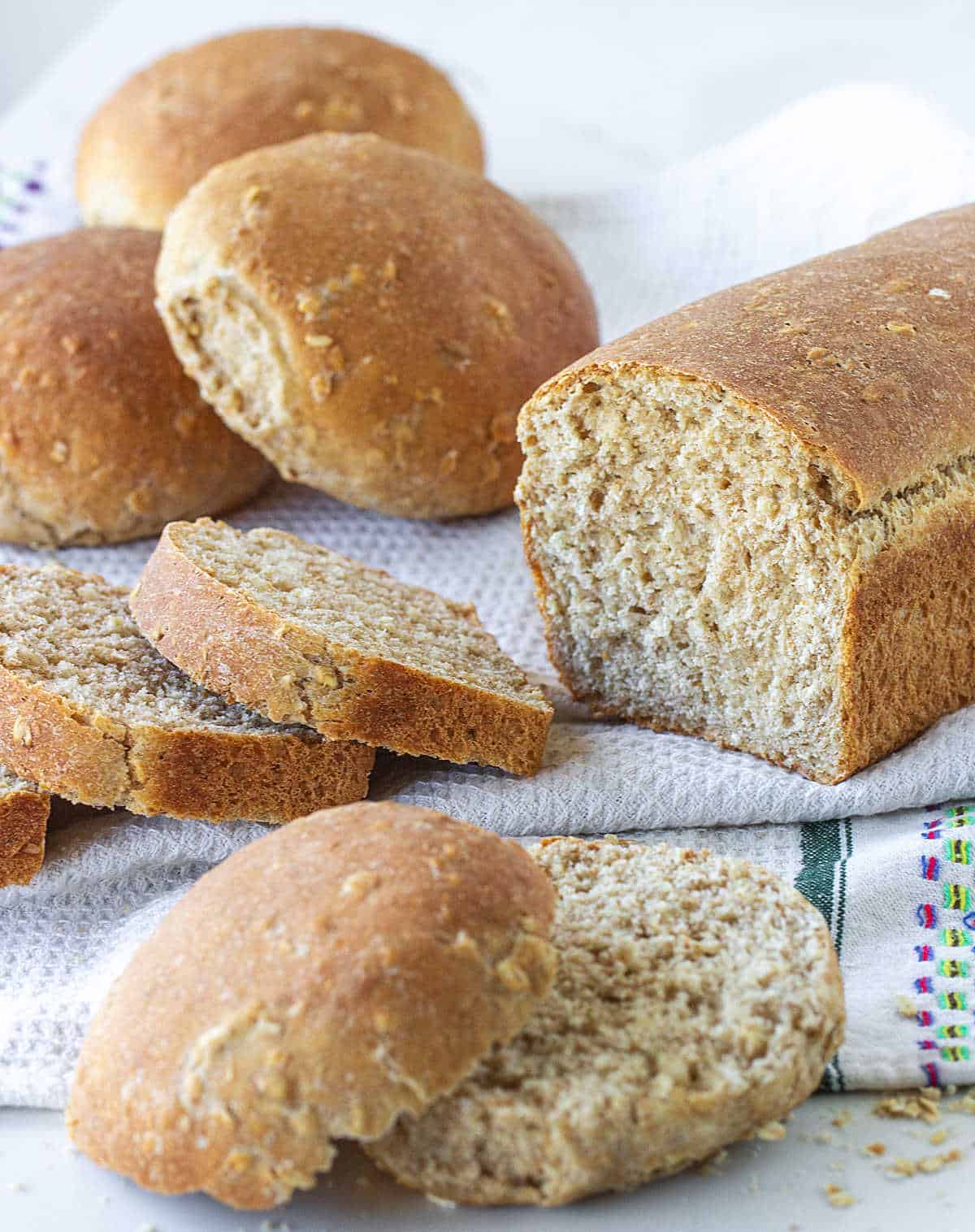 A loaf bread and buns on a white kitchen towel, whole and sliced.