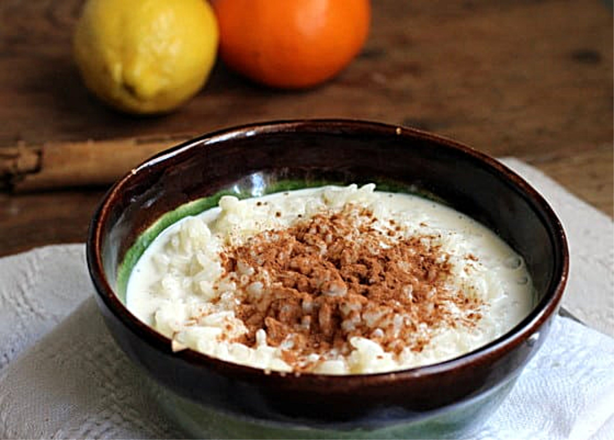 Dark bowl with rice pudding, wooden table, citrus fruit.