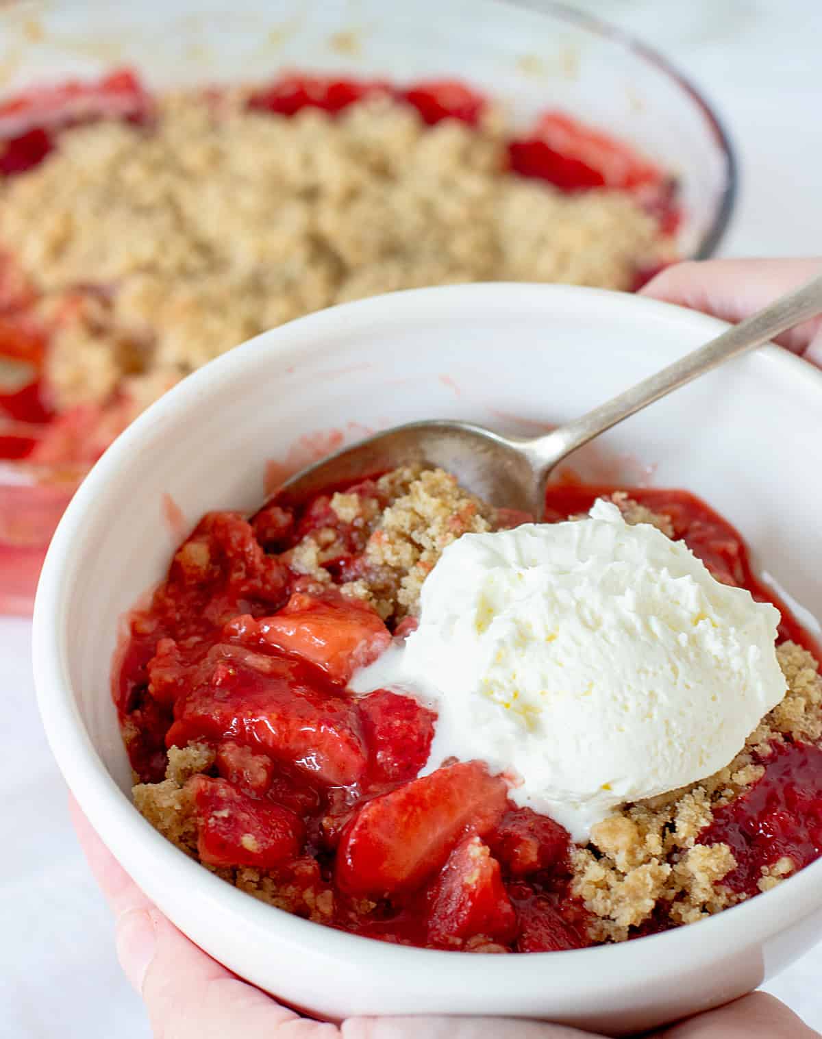 White bowl with strawberry crisp and ice cream, silver spoon.
