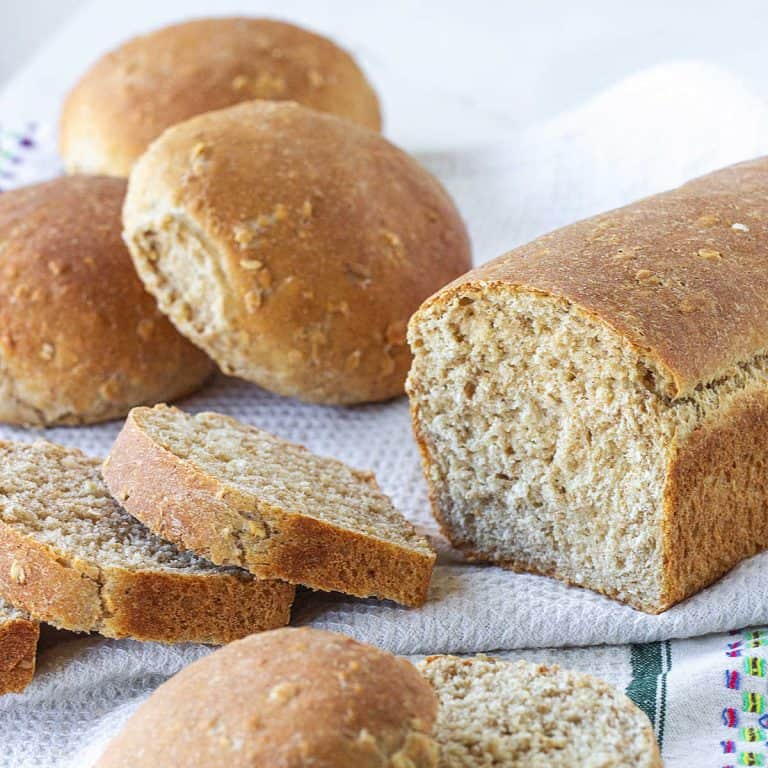 Sliced and half loaf of bread and hamburger buns on a white kitchen towel.