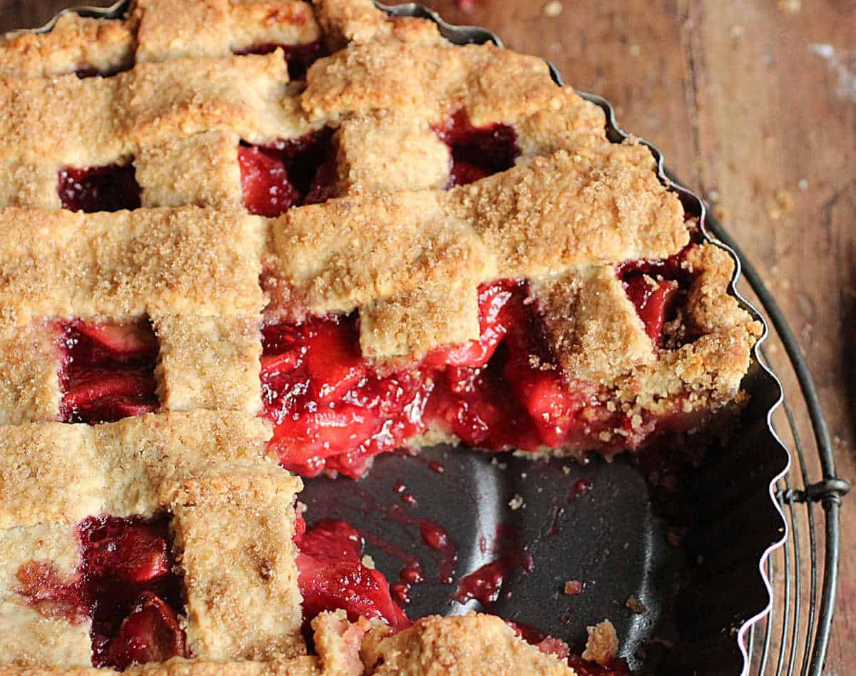 Close up of partial apple raspberry lattice pie on a dark metal pan on a wooden table.