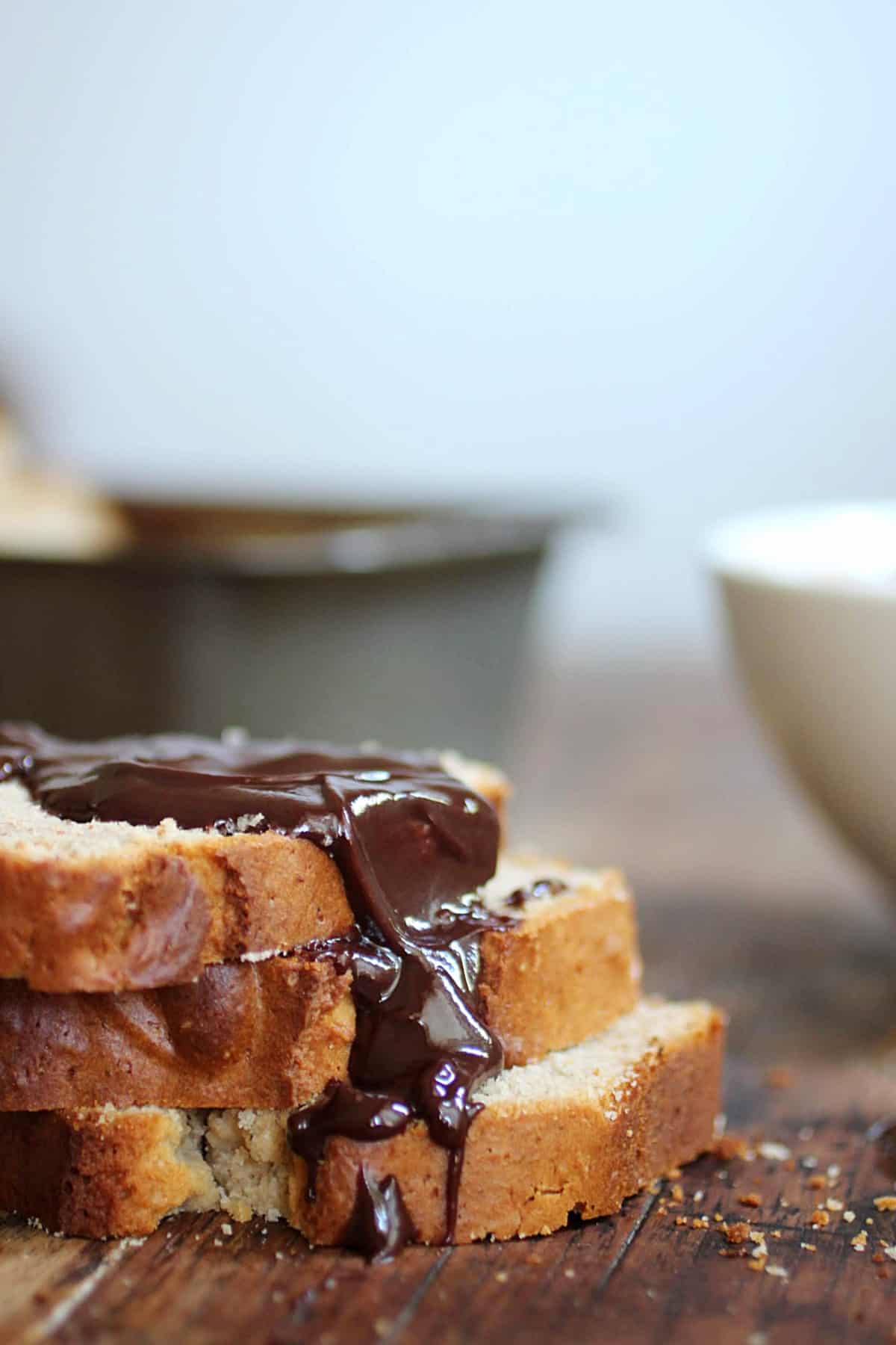 Stack of quick bread slices with chocolate sauce, wooden table, metal pan in background