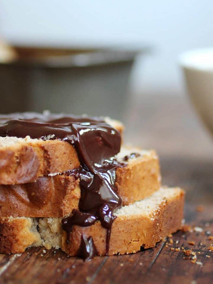 Stack of quick bread slices with chocolate sauce, wooden table, metal pan in background