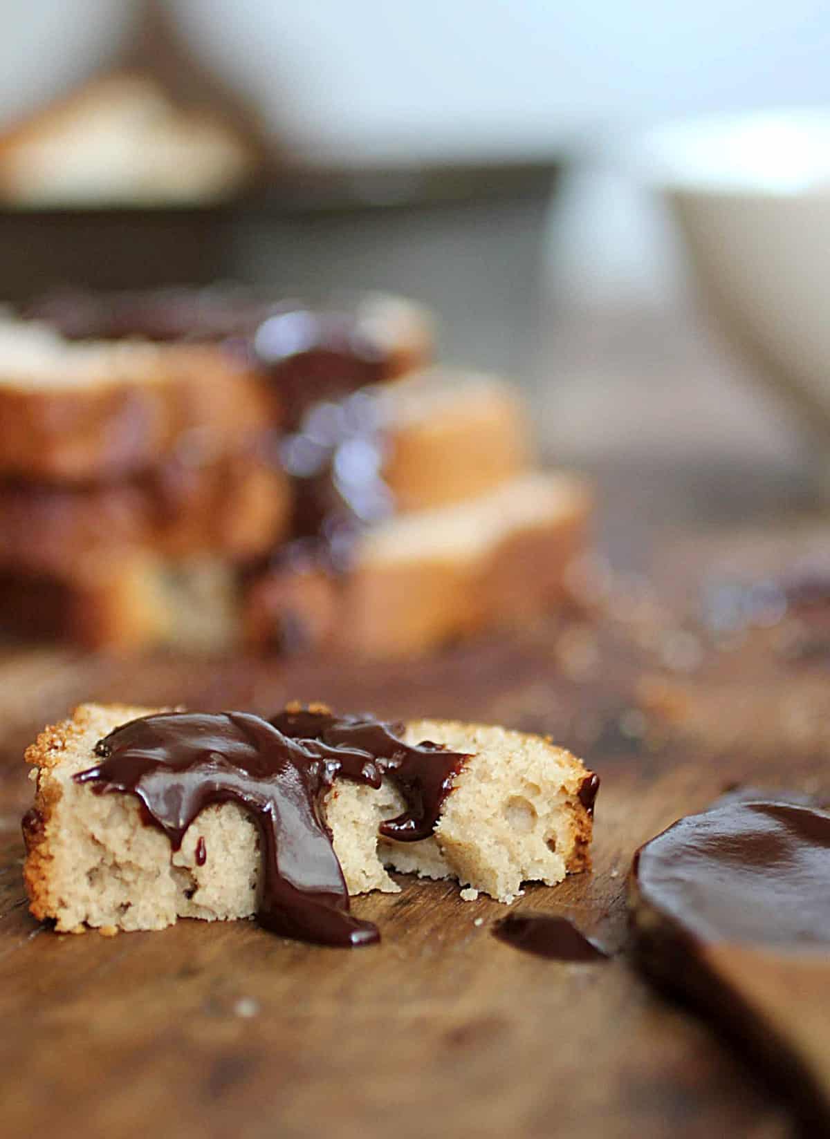 Half slice of peanut butter bread with chocolate sauce on wooden board, stack of slices, wooden spoon in background