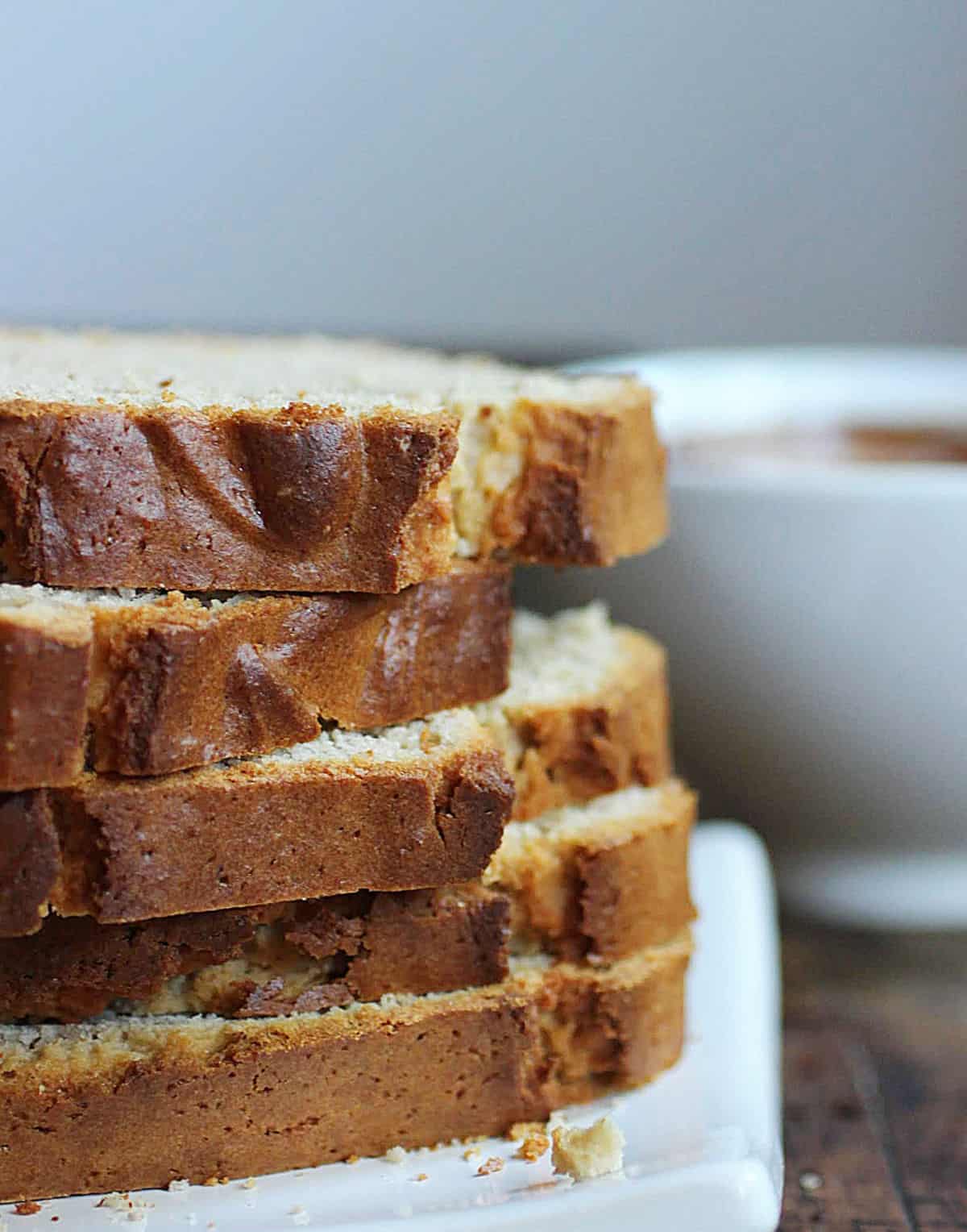 Several slices of peanut butter bread in a stack on a white plate. White bowl in the grey background. 