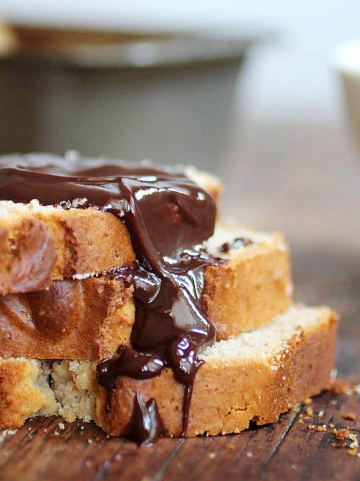 Three slices of peanut butter bread in a stack with chocolate sauce on a wooden table. Loaf pan in the background.