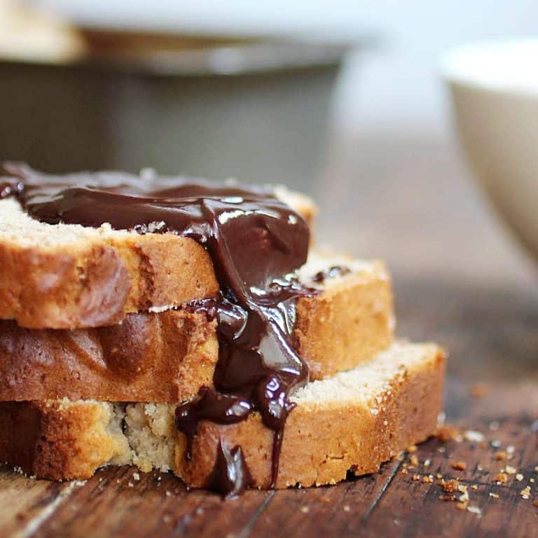 Three slices of peanut butter bread in a stack with chocolate sauce on a wooden table. Loaf pan in the background.
