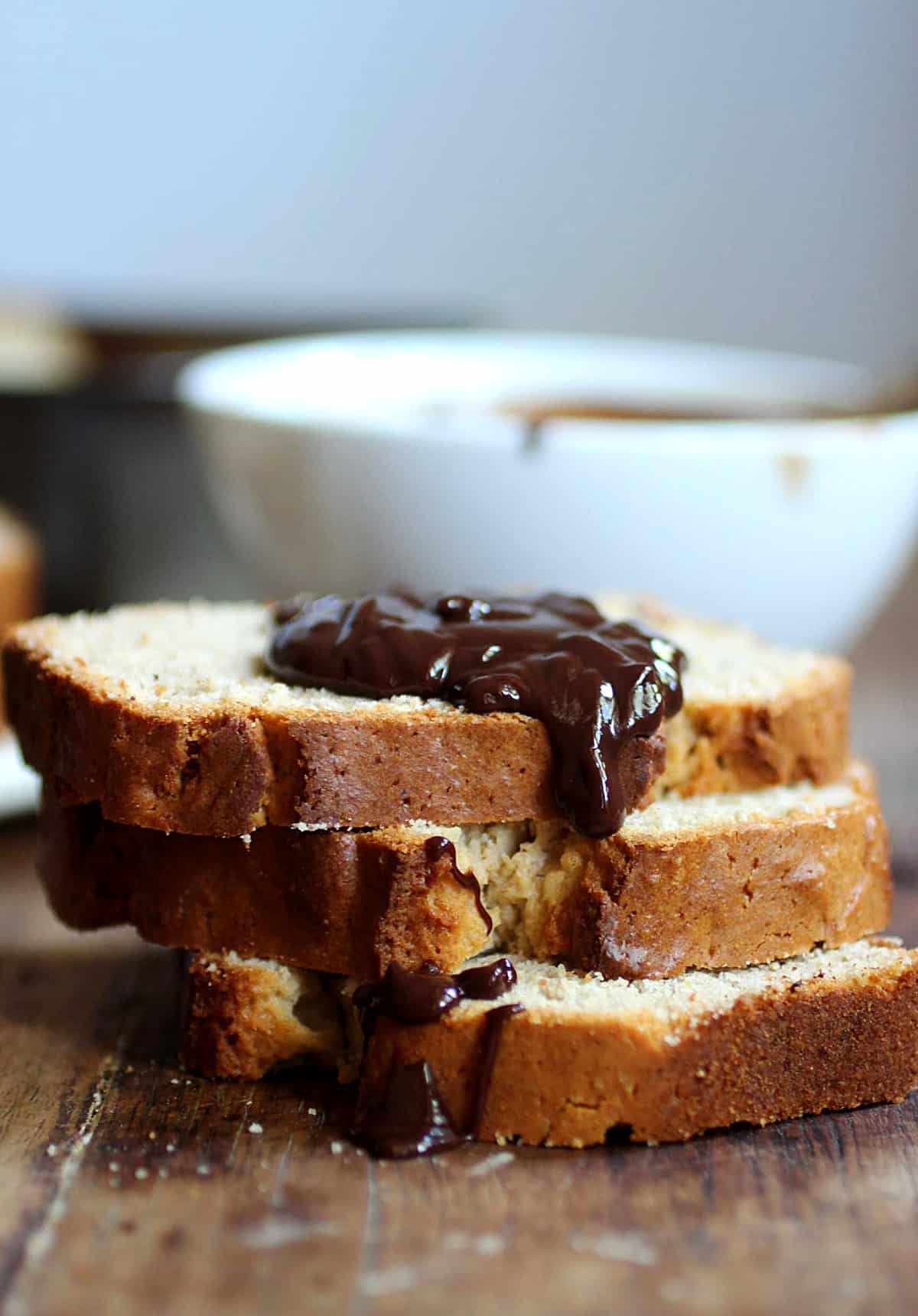 Slice of quick bread with chocolate sauce, wooden table, white bowl