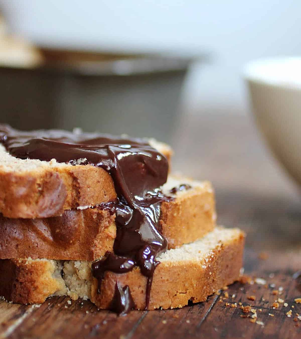 Stack of peanut butter quick bread slices with chocolate sauce, wooden table, metal pan in background.
