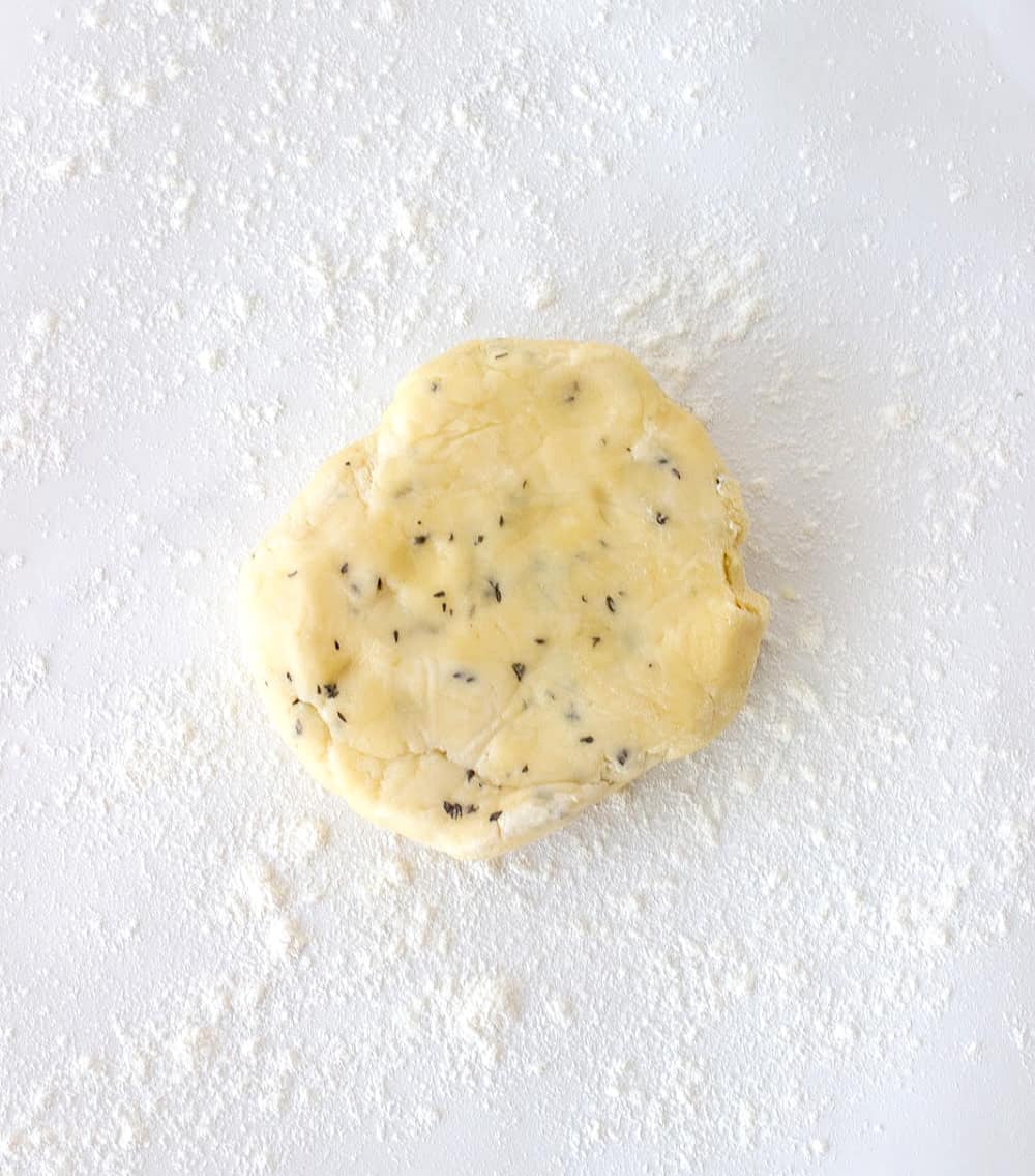 Round of herbed pie dough on a floured white surface.