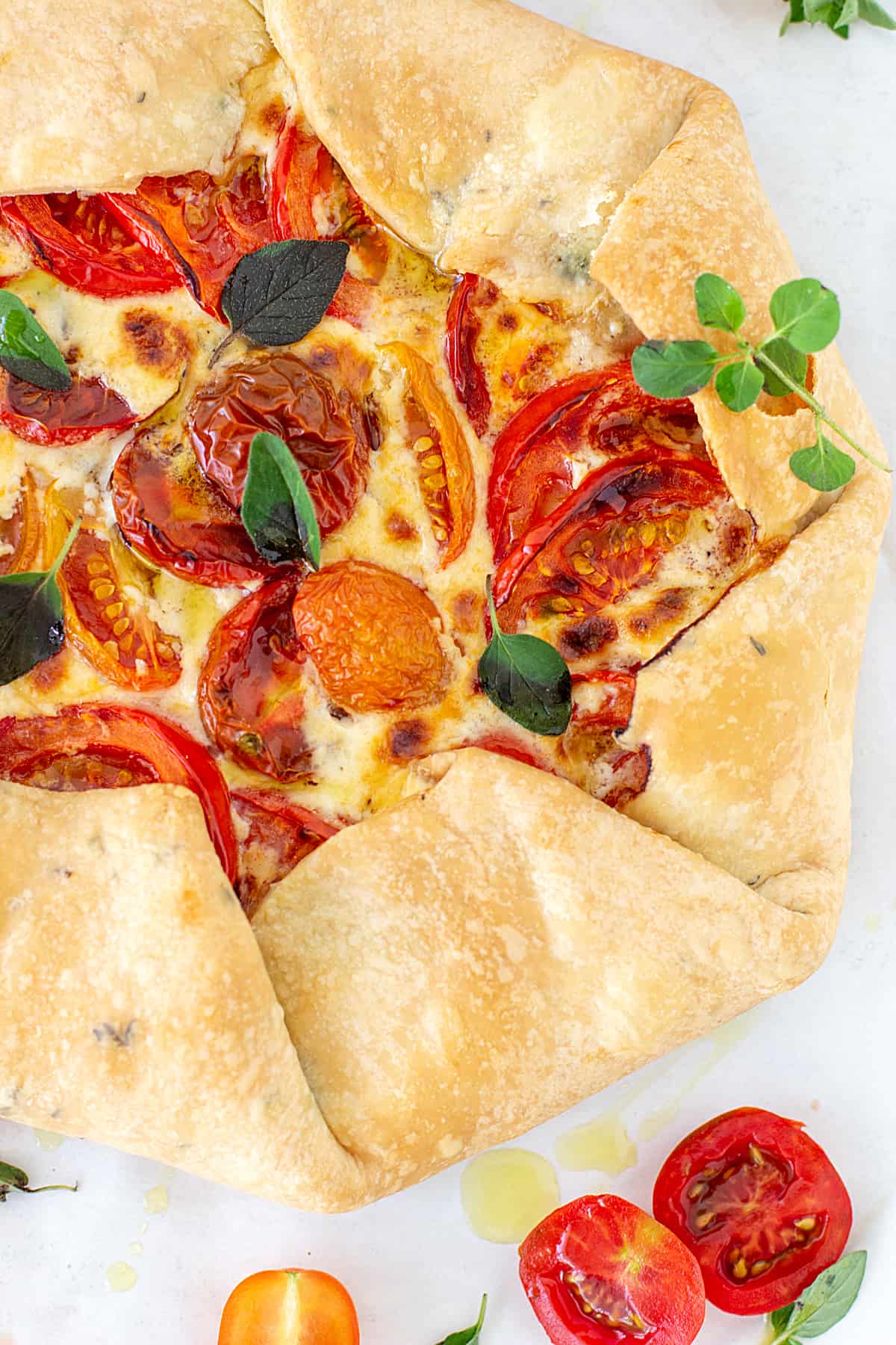 Partial image of tomato free-form pie on white surface, loose herbs around.