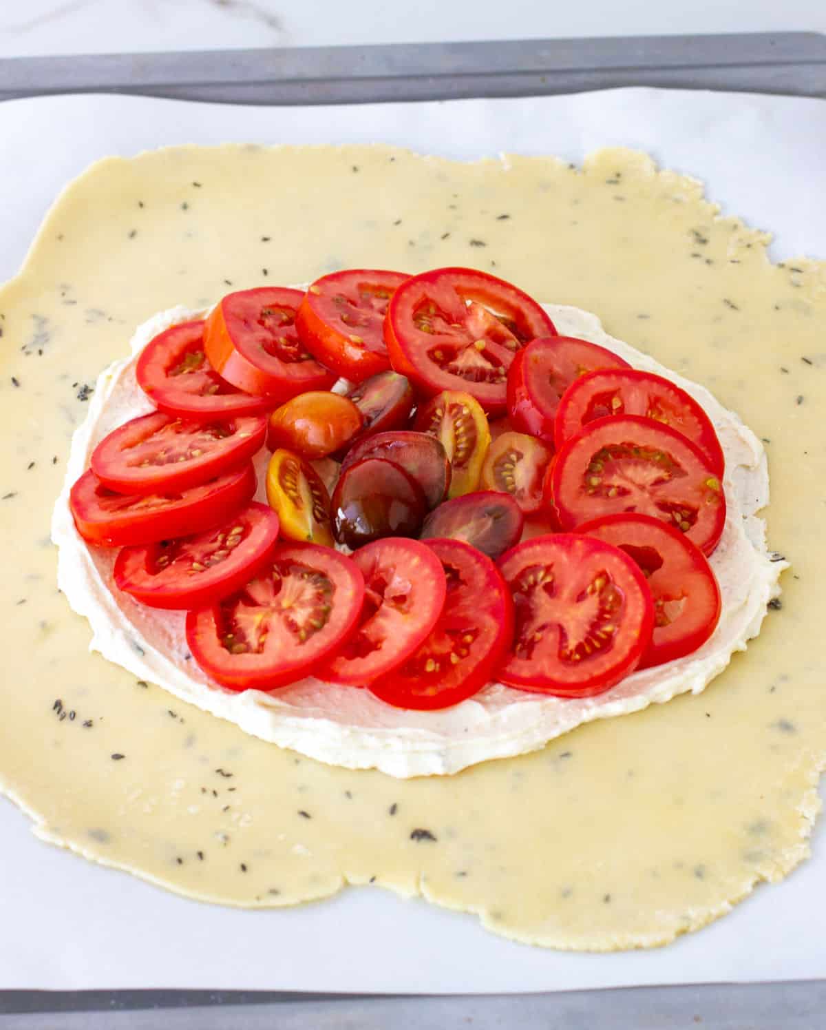 Tomato and cheese filling in center of herbed pie crust round on white parchment paper.