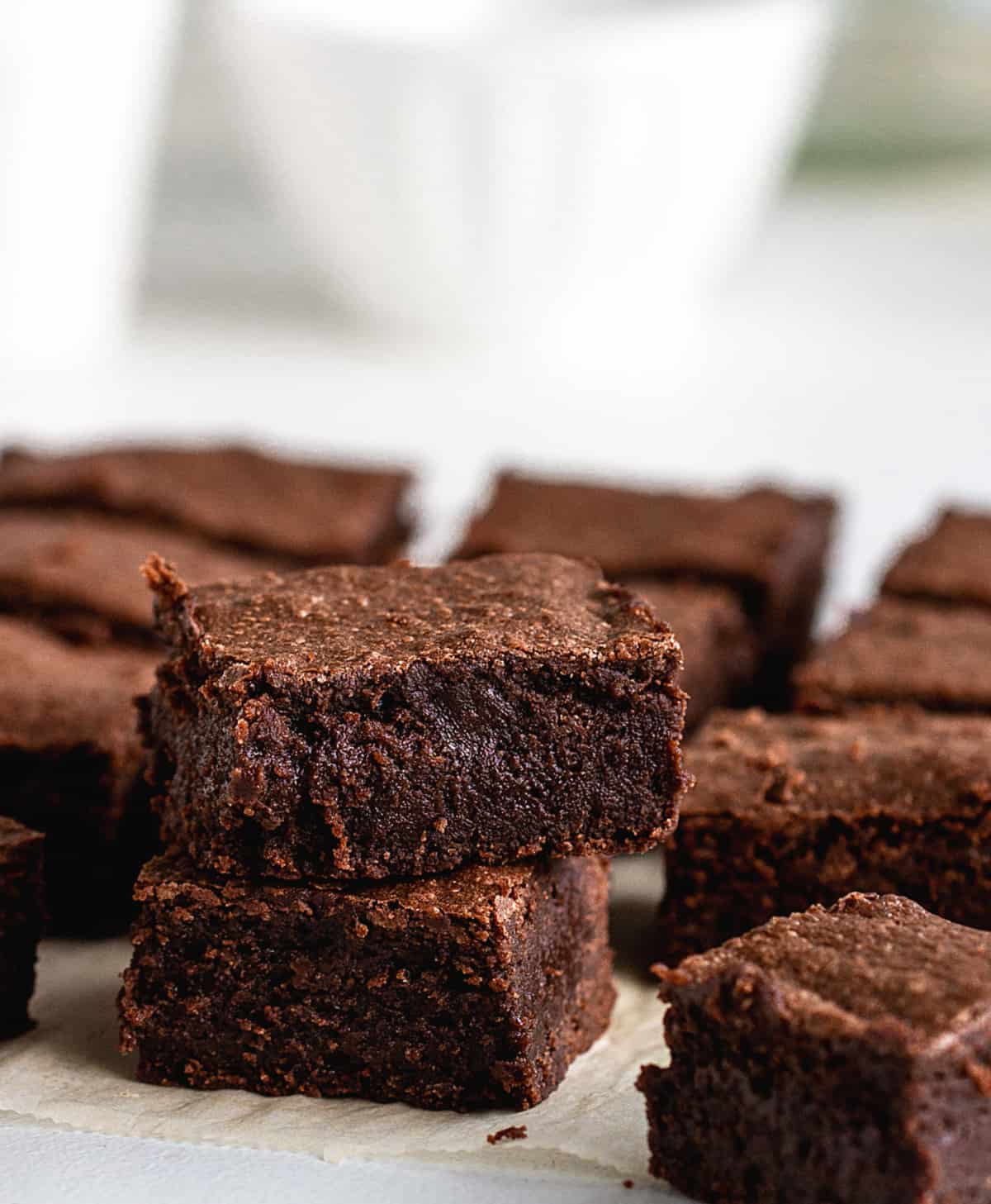 Lots of brownie squares on white surface, white bowl on background.