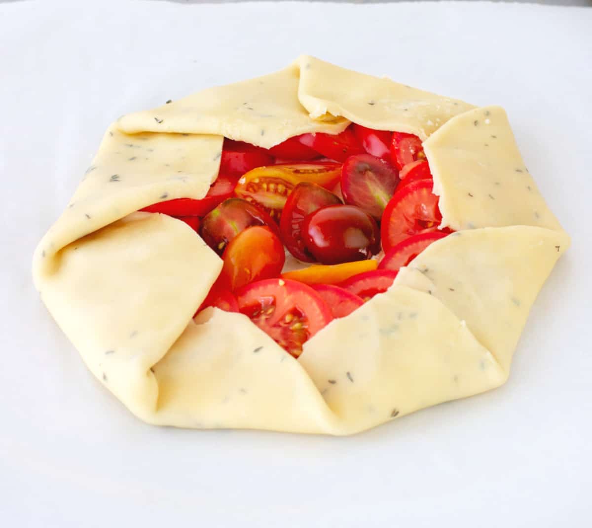 Unbaked tomato galette on white parchment paper.