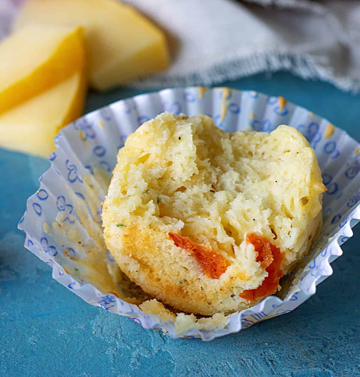 Paper cup with half eaten muffin, blue background with slices of cheese as props