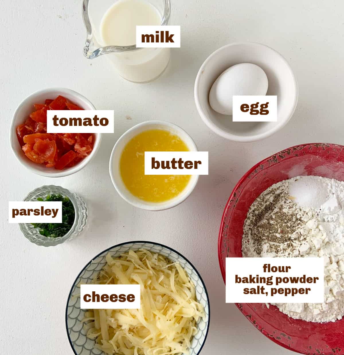 Bowls with cheese, tomato, and other basic ingredients on a white surface