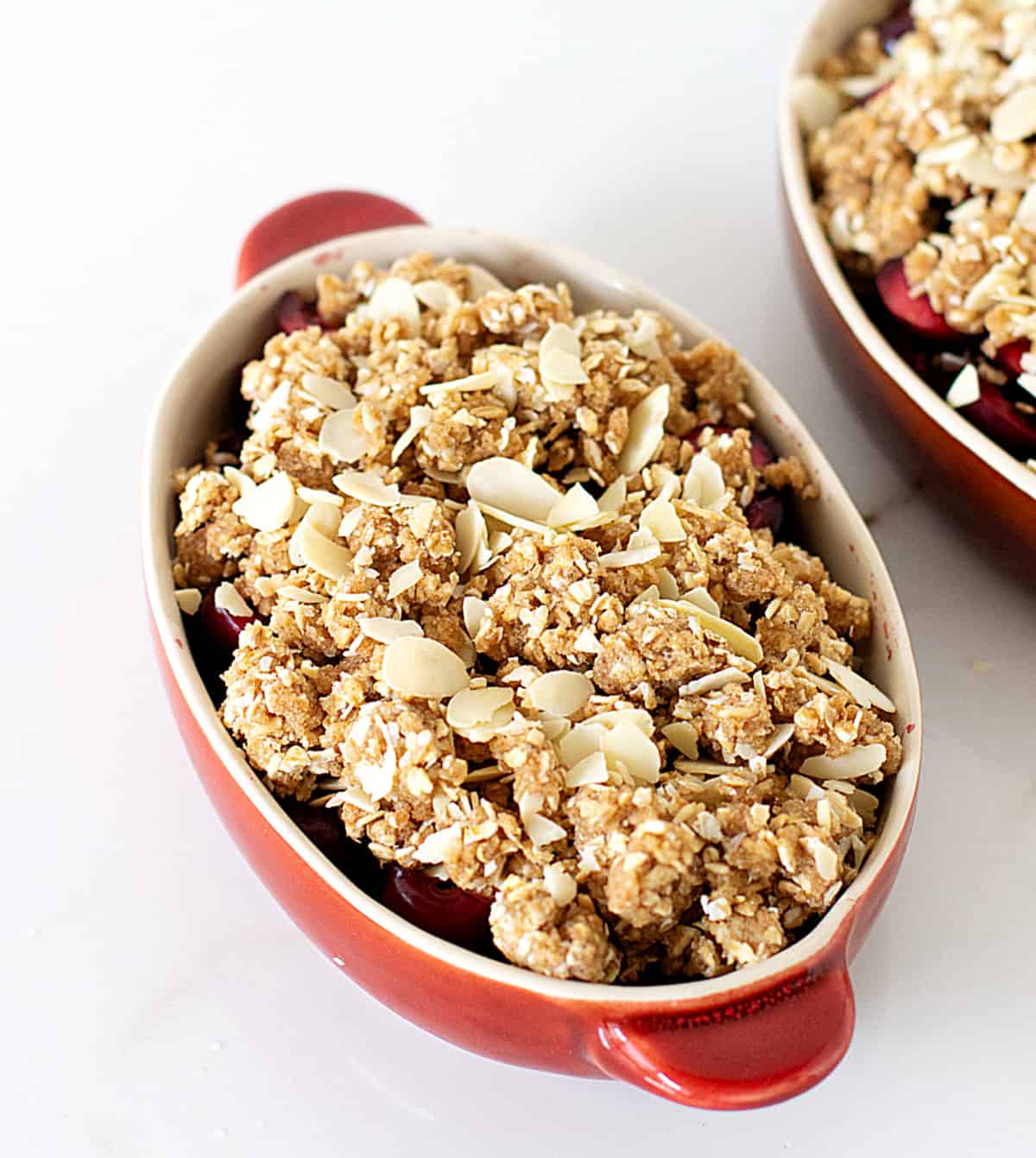 Unbaked cherry oat crumble in red oval dish on white table.