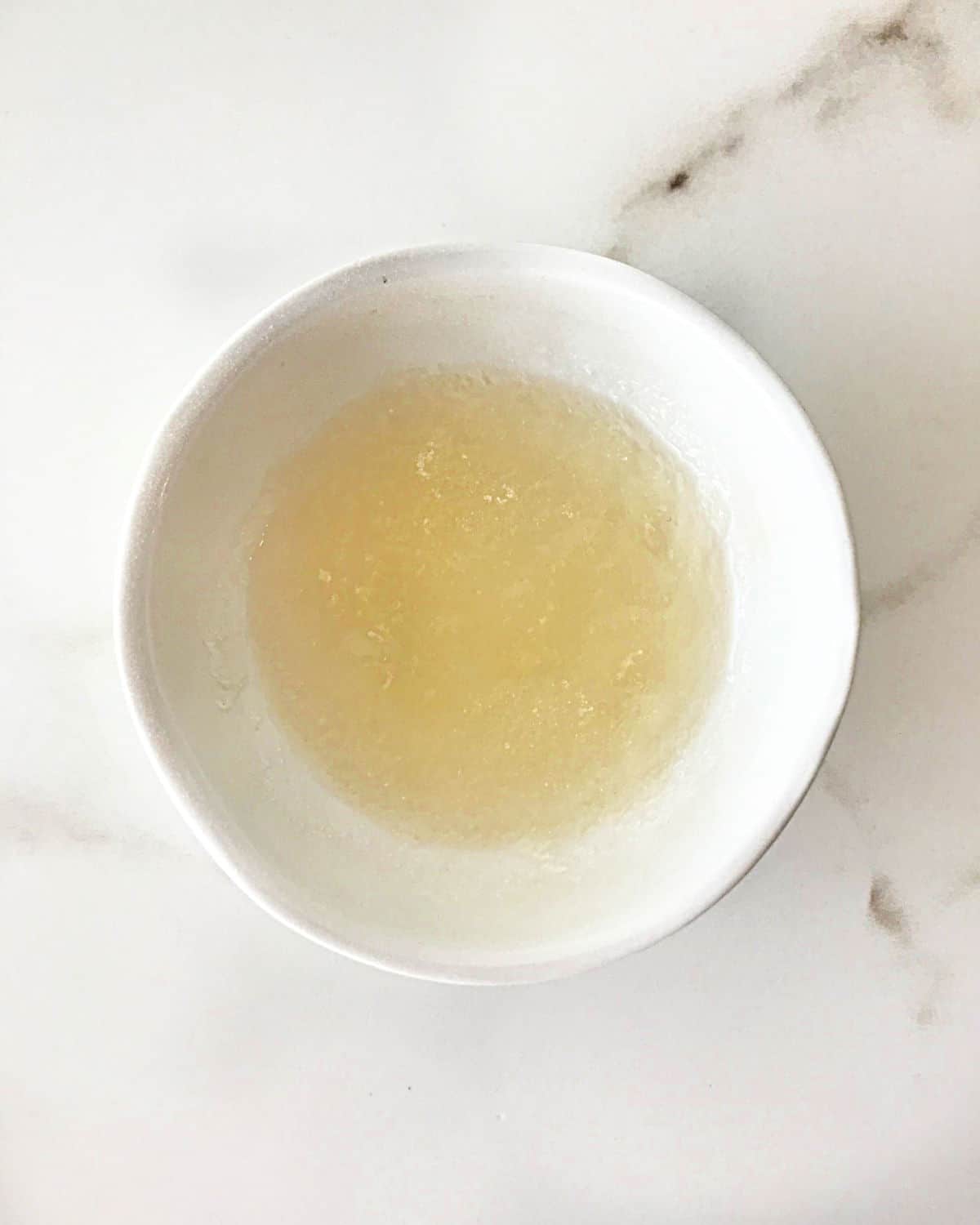 Small white bowl with hydrated gelatin on a white marble surface.