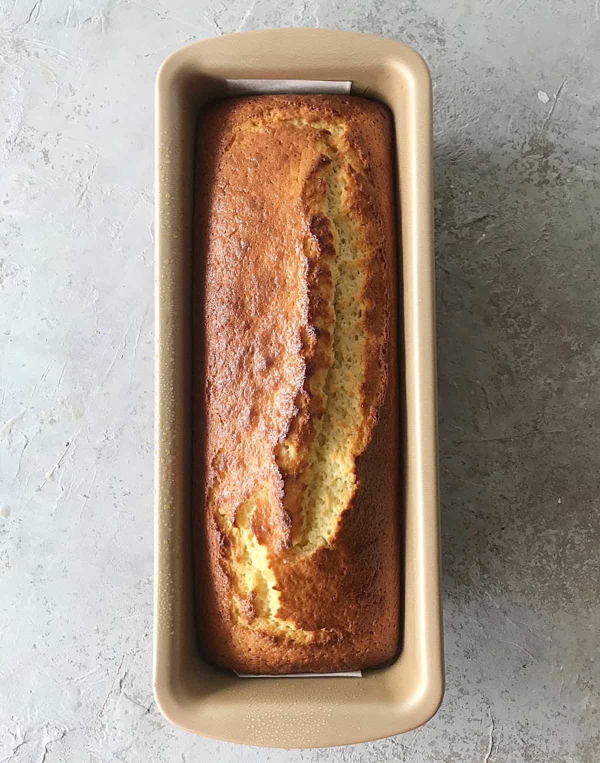 Golden loaf pan with baked cake, grey surface.