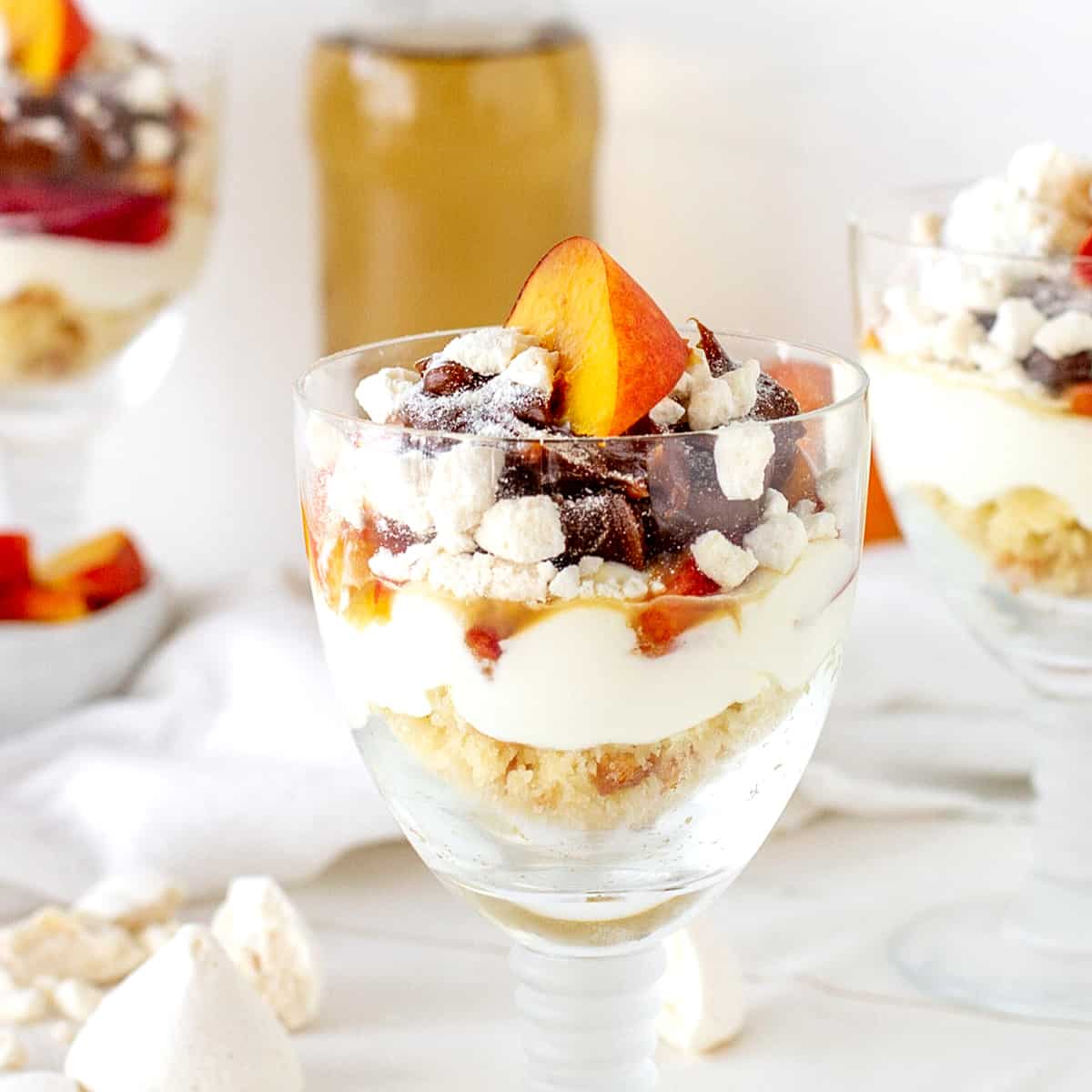 Several glass cups with creamy peach dessert, white surface, bottle with yellow liquid on background.