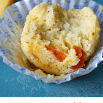 Close-up of half eaten muffin on a white paper cup, blue surface; image with text