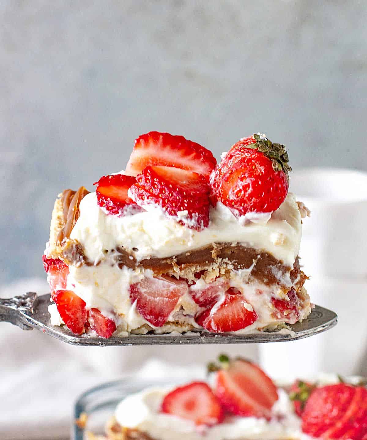 A serving of strawberries and cream icebox cake on a vintage metal cake server on a grey background. 