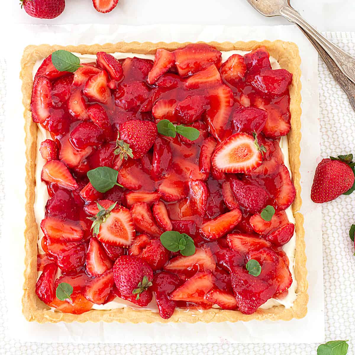 Square strawberry tart with mint leaves on a white surface.