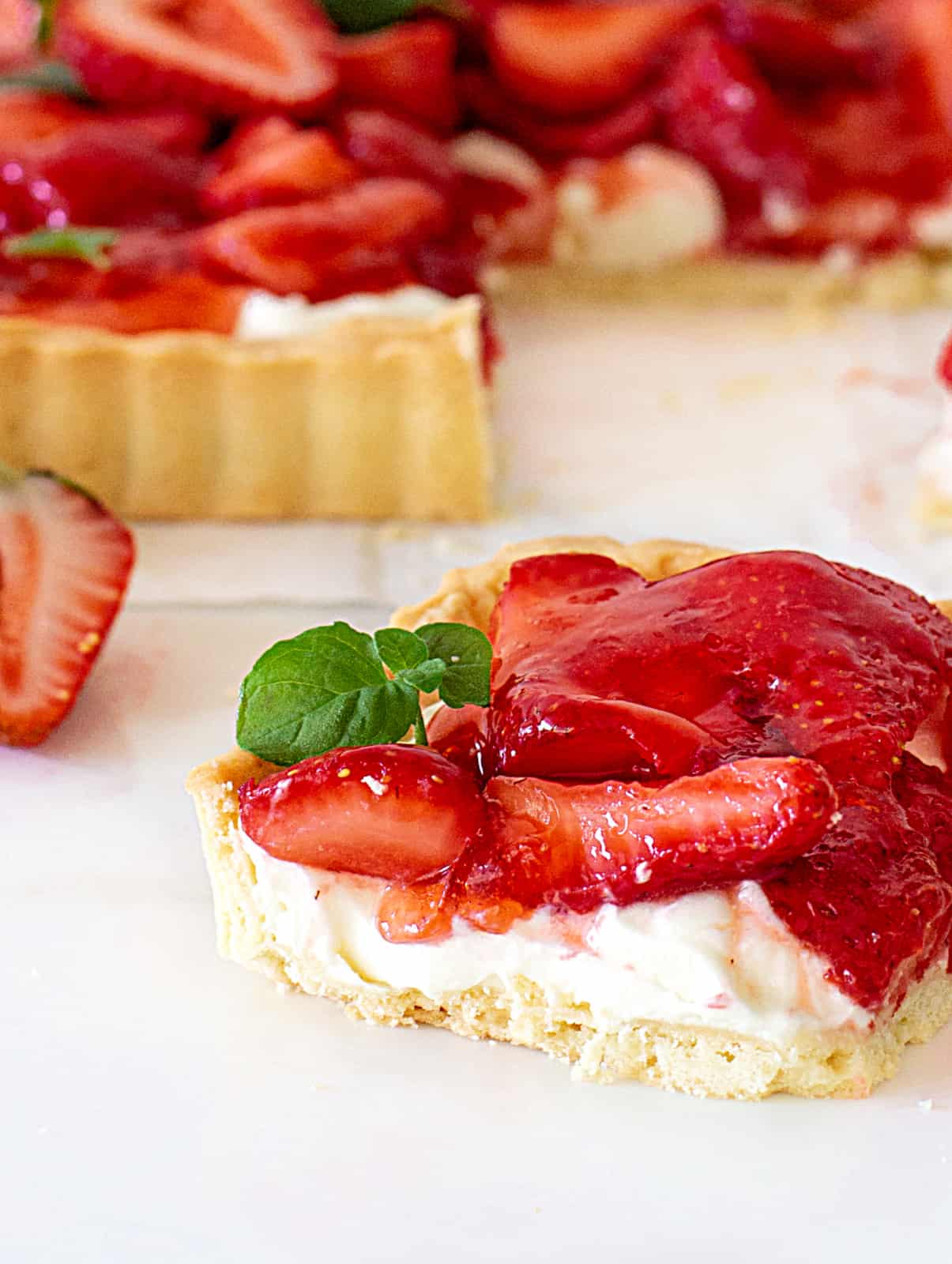 Close-up of square of strawberry cream tart, white surface, mint leaves.