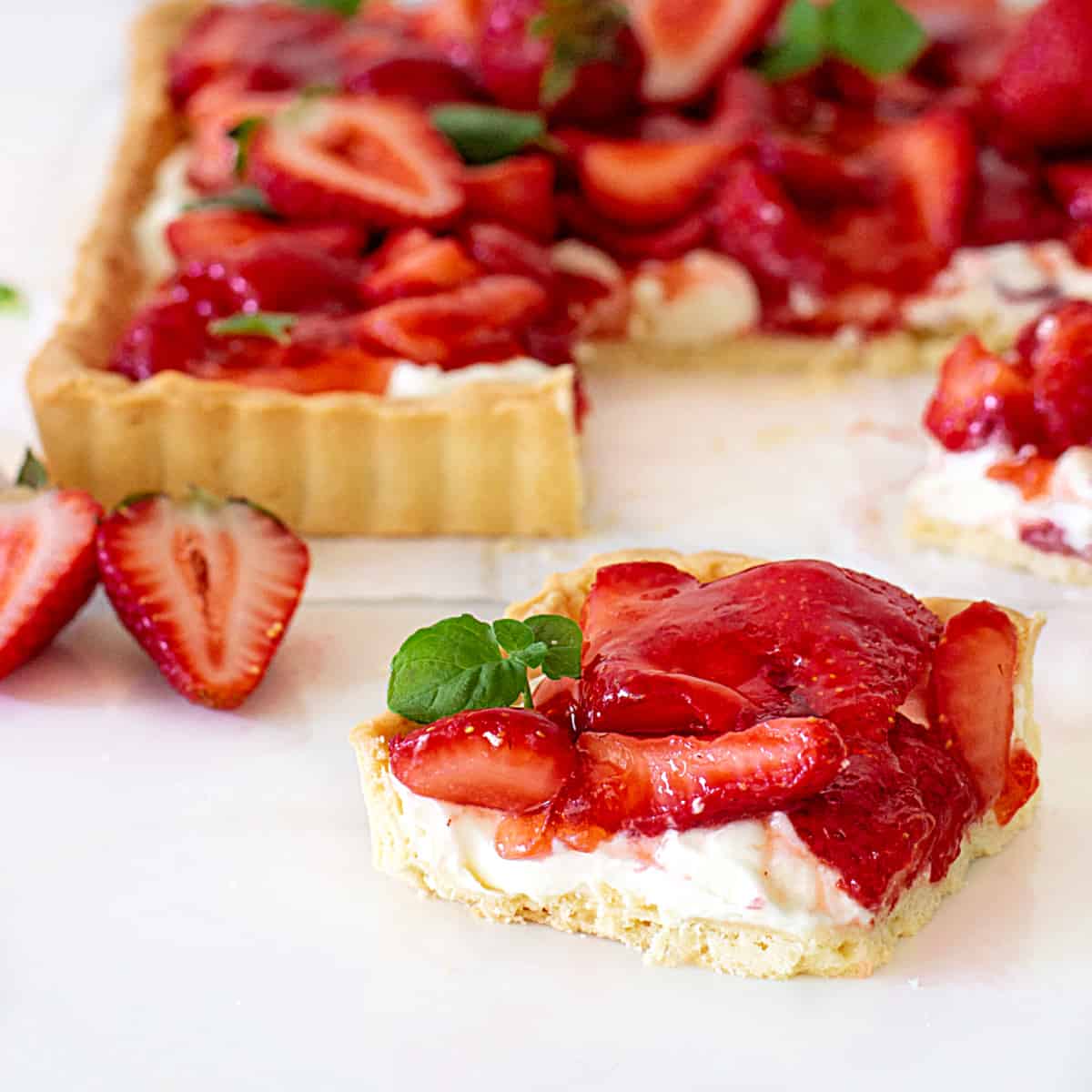 Slice of strawberry tart on white surface, rest of pie in background.