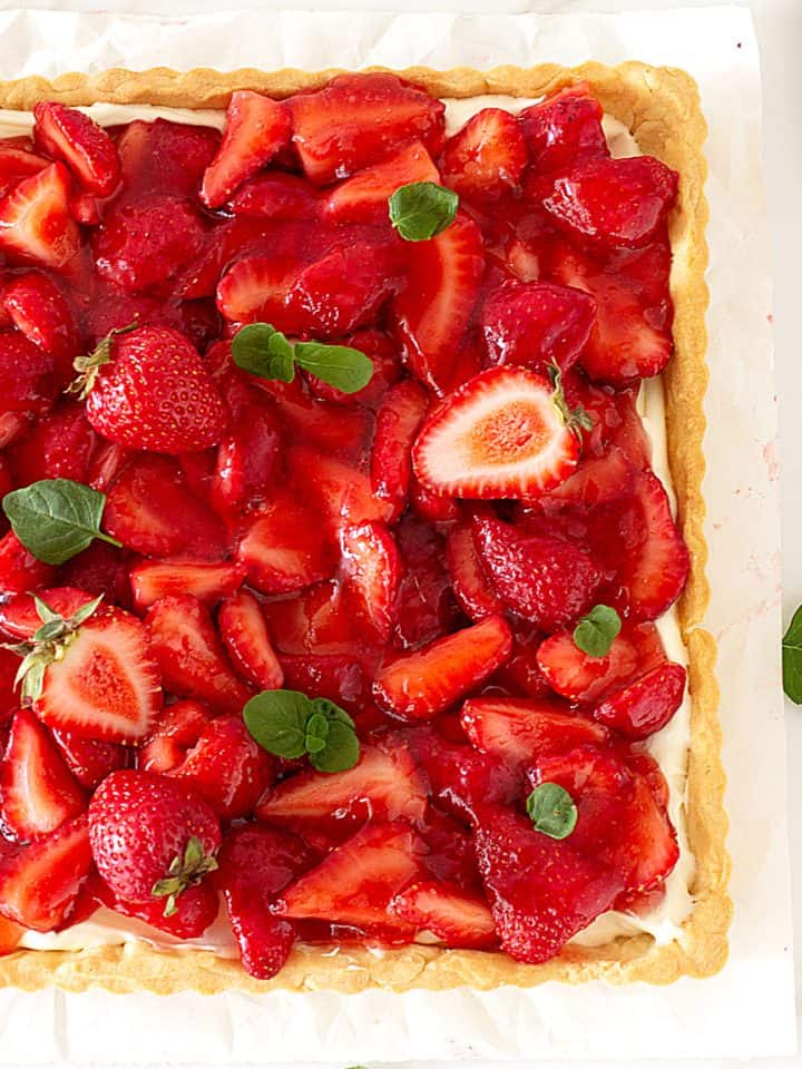 Partial view of strawberry tart on white surface, mint leaves and fork beside