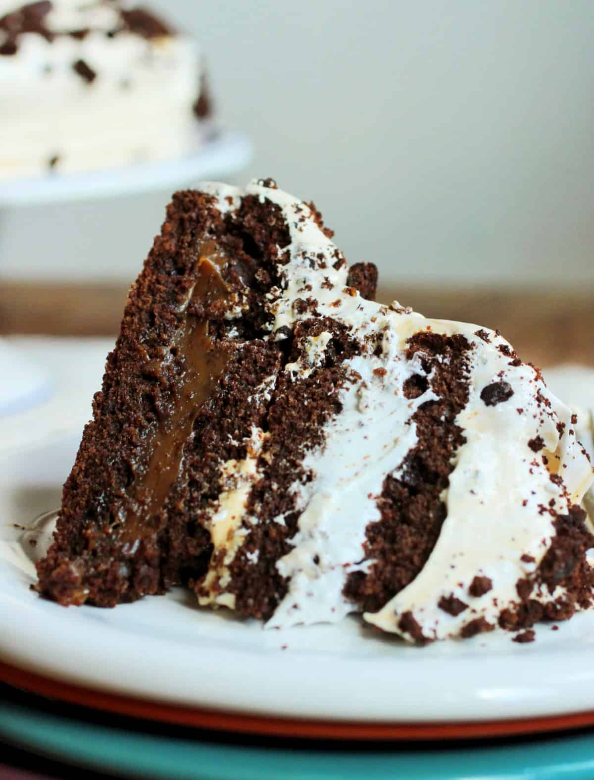 Slice of chocolate meringue layer cake on stack of white and color plates; cake in grey background.