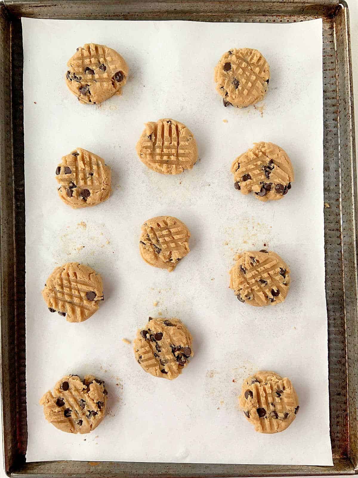 Metal sheet with parchment paper and criss crossed chocolate chip cookies.