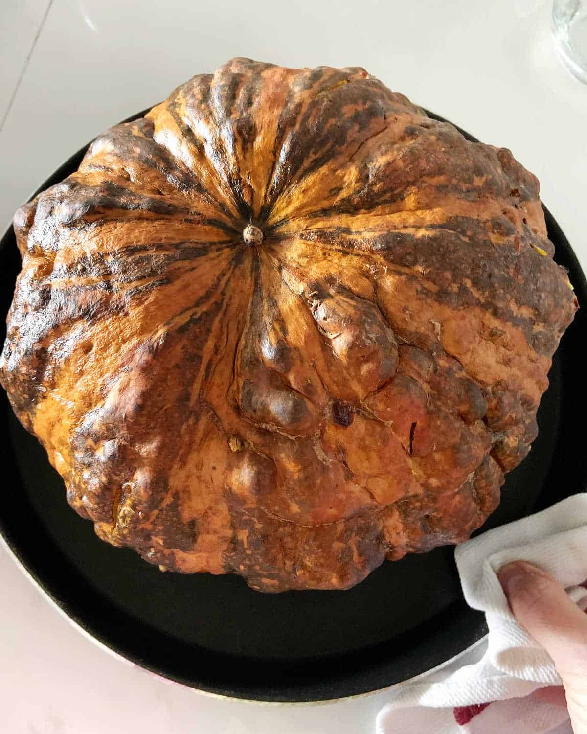 Whole baked pumpkin on a dark round pan on a white surface.