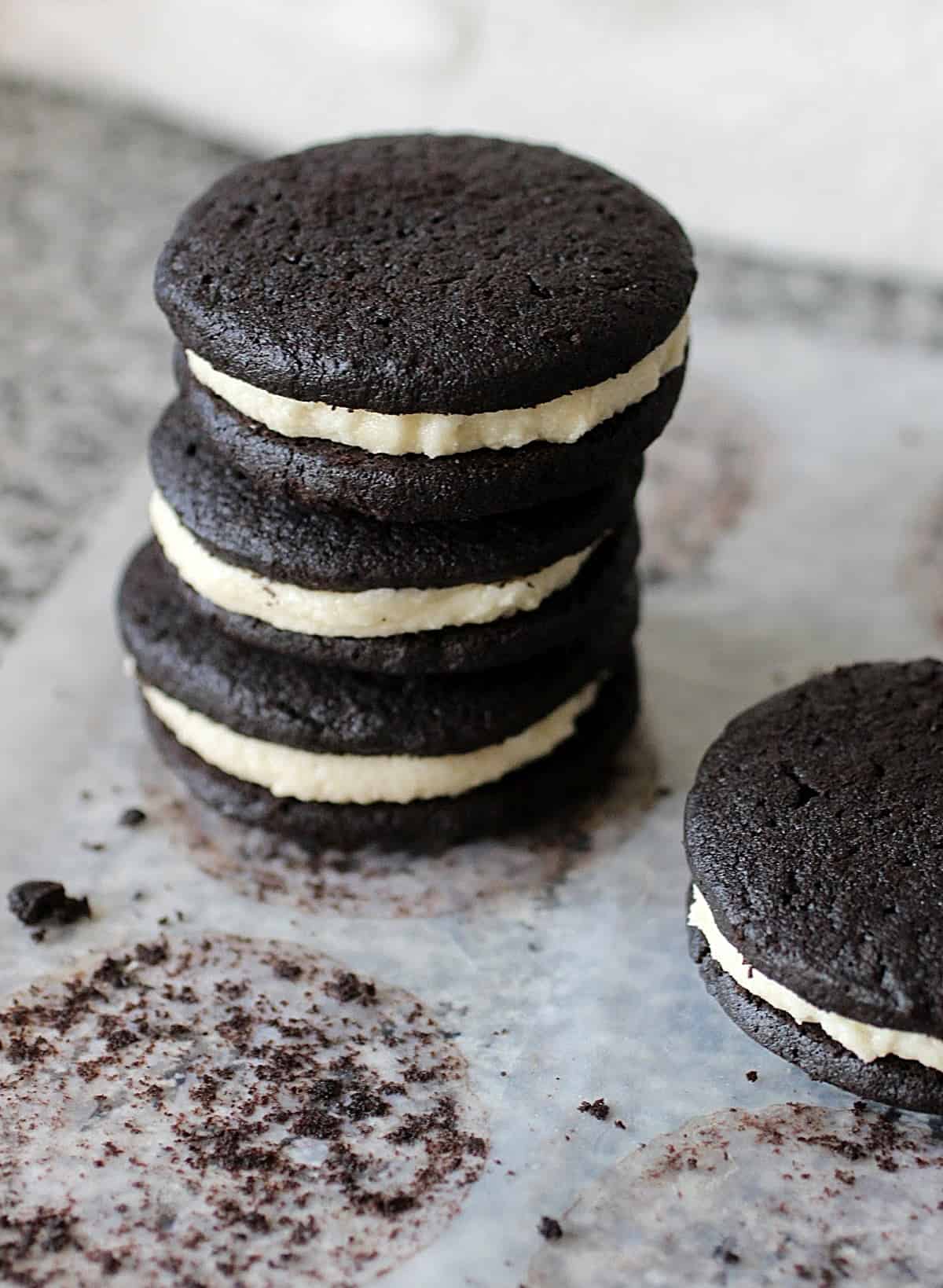 Grey surface with a stack of three filled chocolate cookies, partial view of another cookie