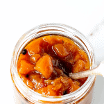 Peach chutney in glass jar with silver spoon on a white surface; long pin with text