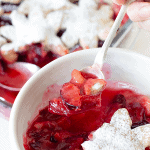 Silver spoon lifting plum cobbler from white bowl, pie crust flower covered in sugar; pin with text