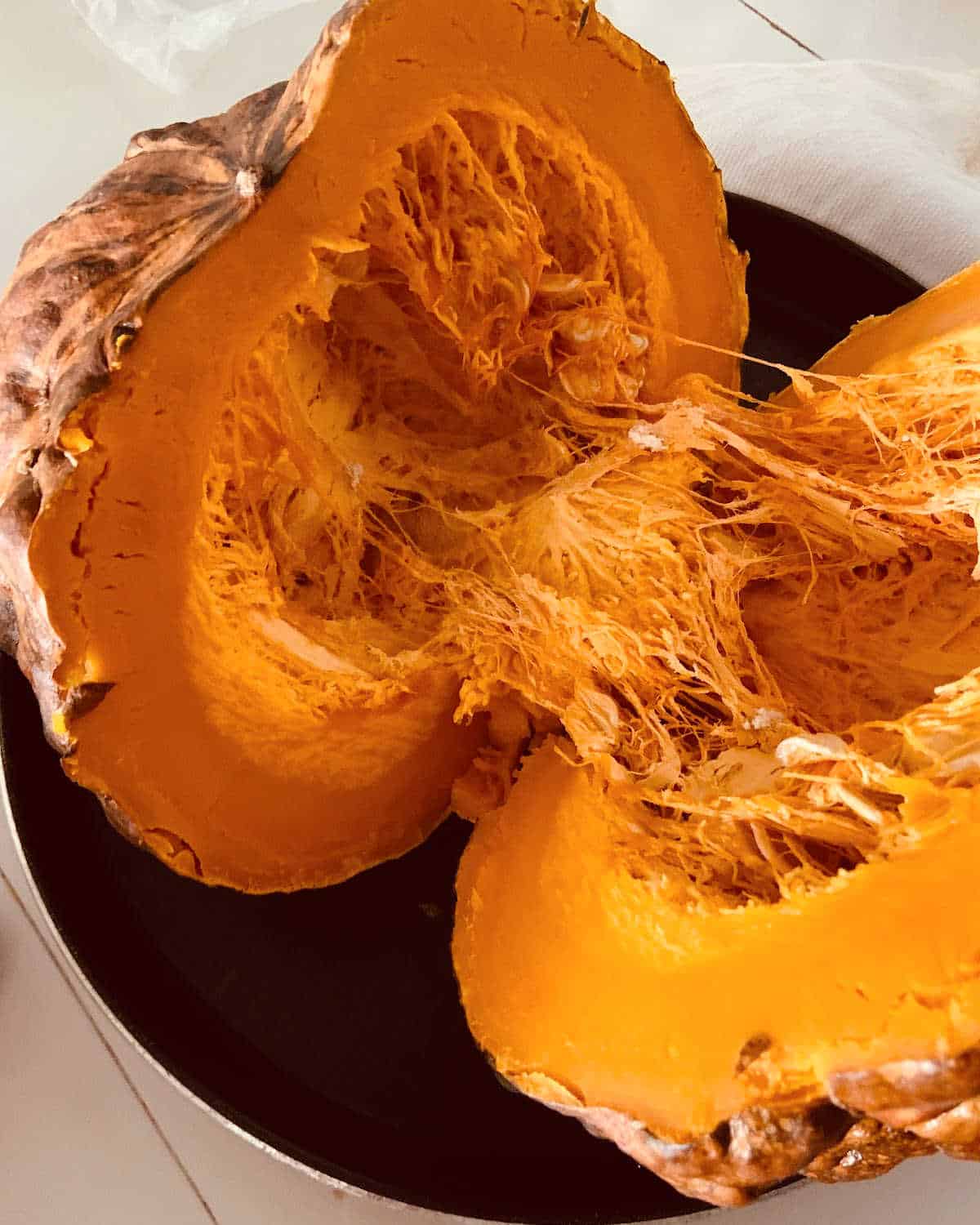 Dark round pan on a white table with opened baked whole pumpkin.