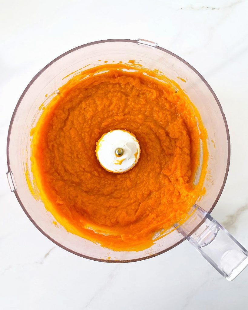 White surface with food processor bowl containing pumpkin puree. Top view.