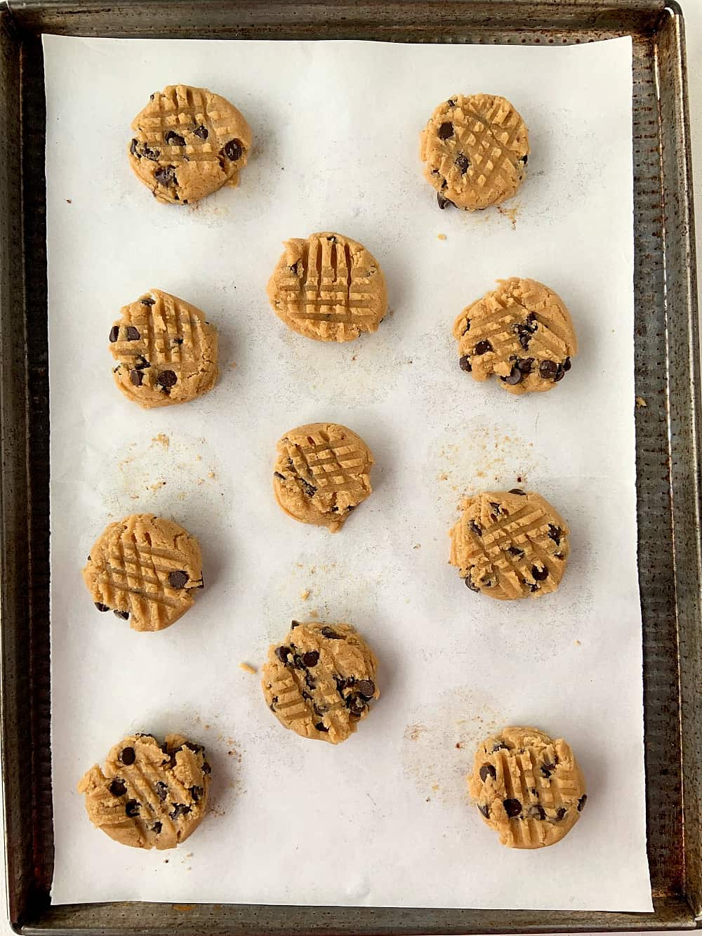Metal cookie tray with unbaked almond butter cookies with chocolate chips on parchment paper. 
