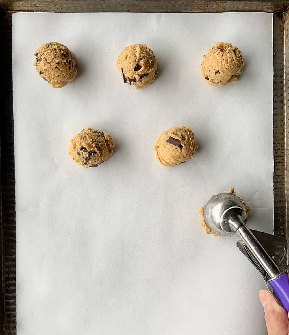 Scooping cookie dough mounds on grey cookie tray with parchment paper