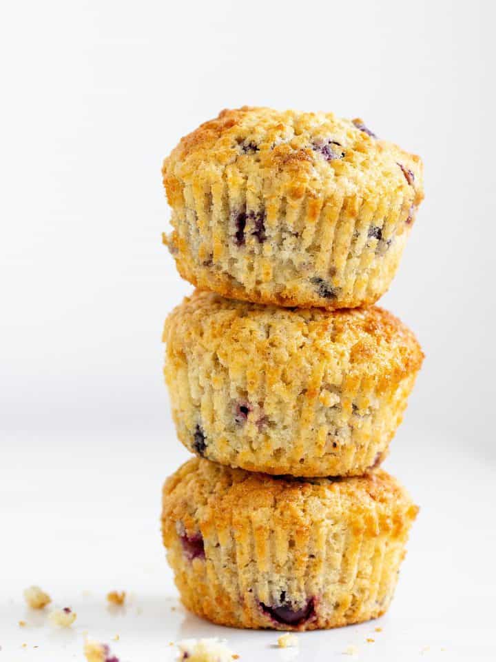 Stack of three golden colored muffins with blueberries, white surface and background