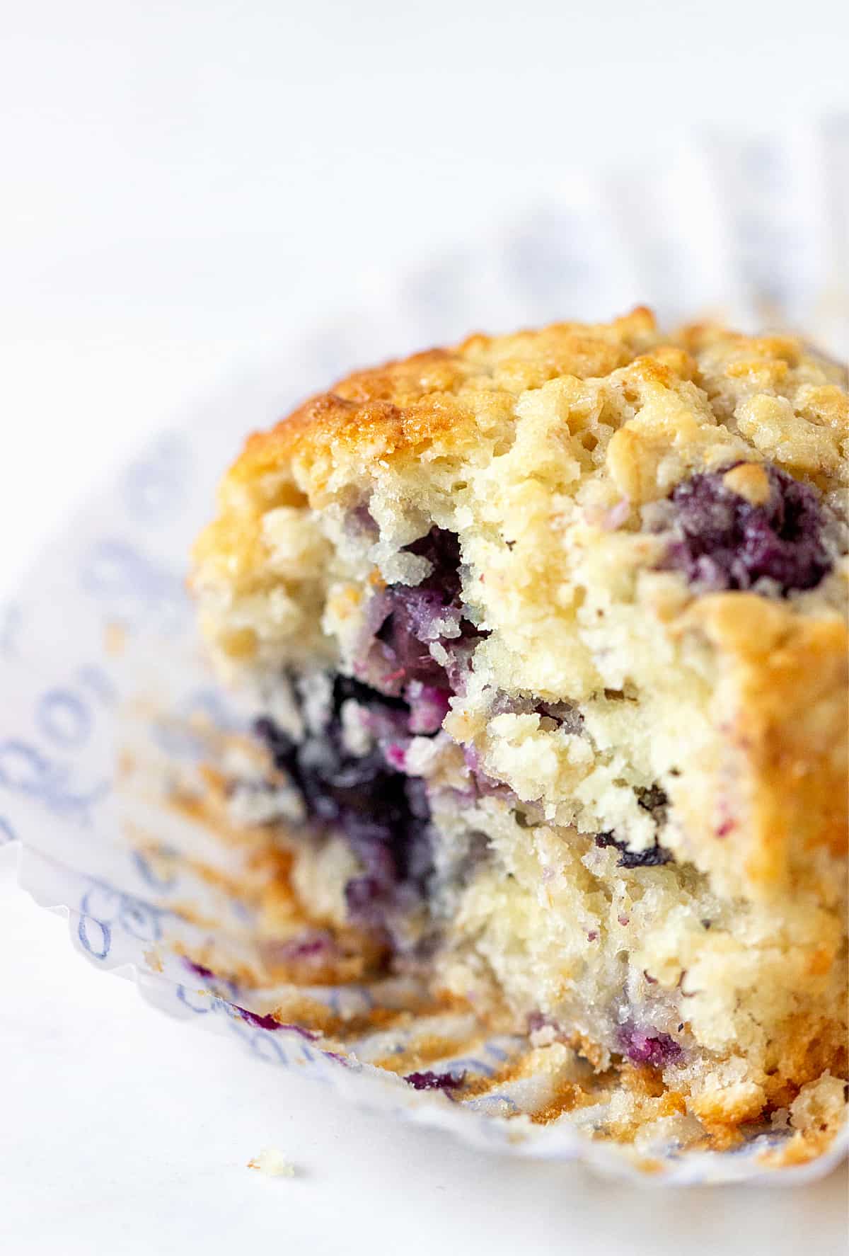 Half blueberry muffin in opened paper cup, white surface