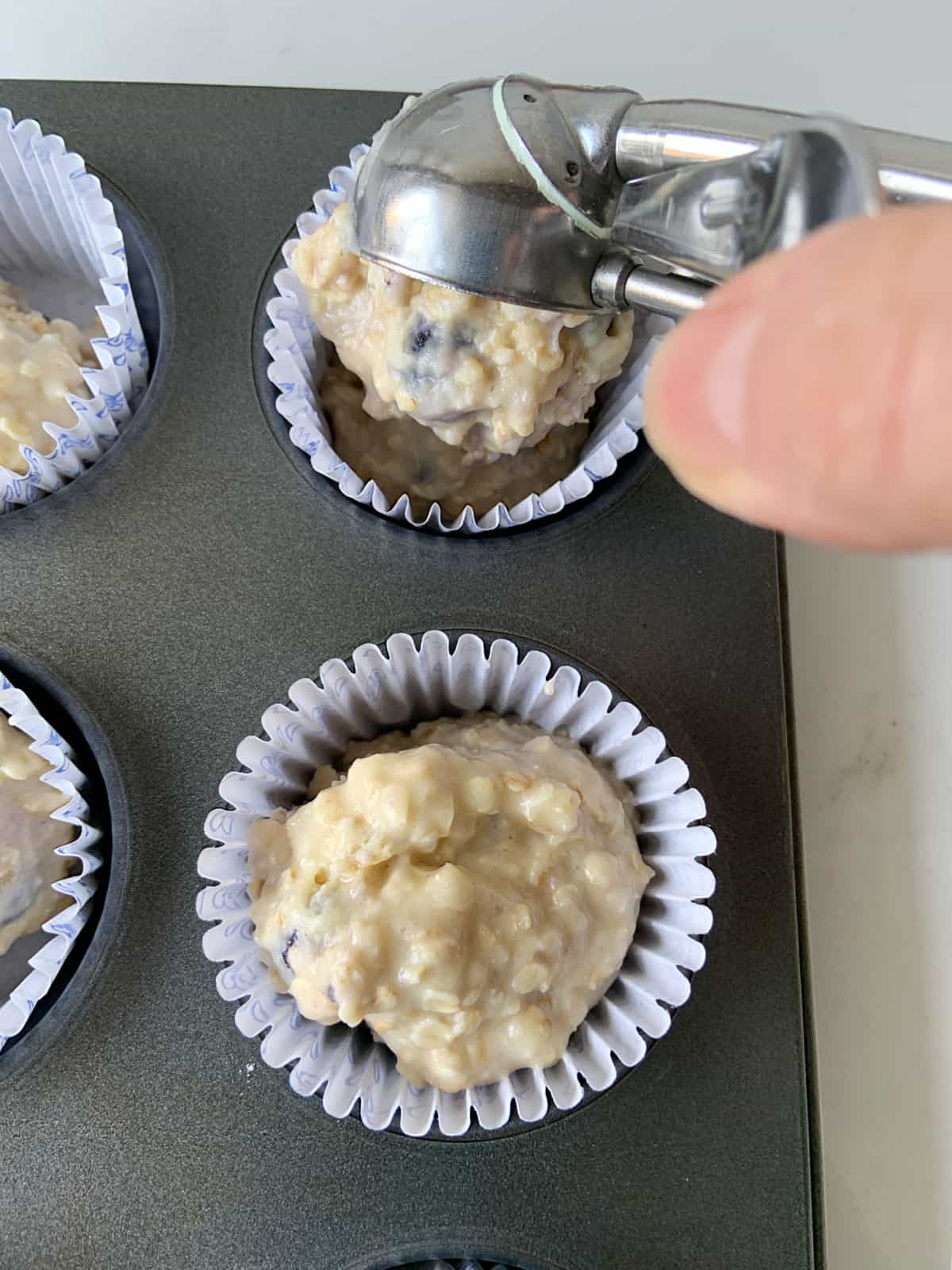 Filling paper cups with muffin batter with scooping spoon