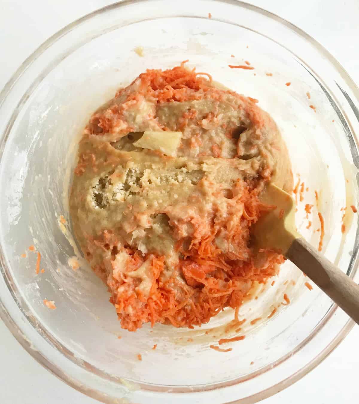Adding shredded carrot and pineapple chunks to cake batter in glass bowl