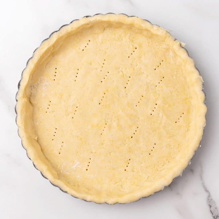 Lined unbaked pie crust in a round pan on a white marbled surface.