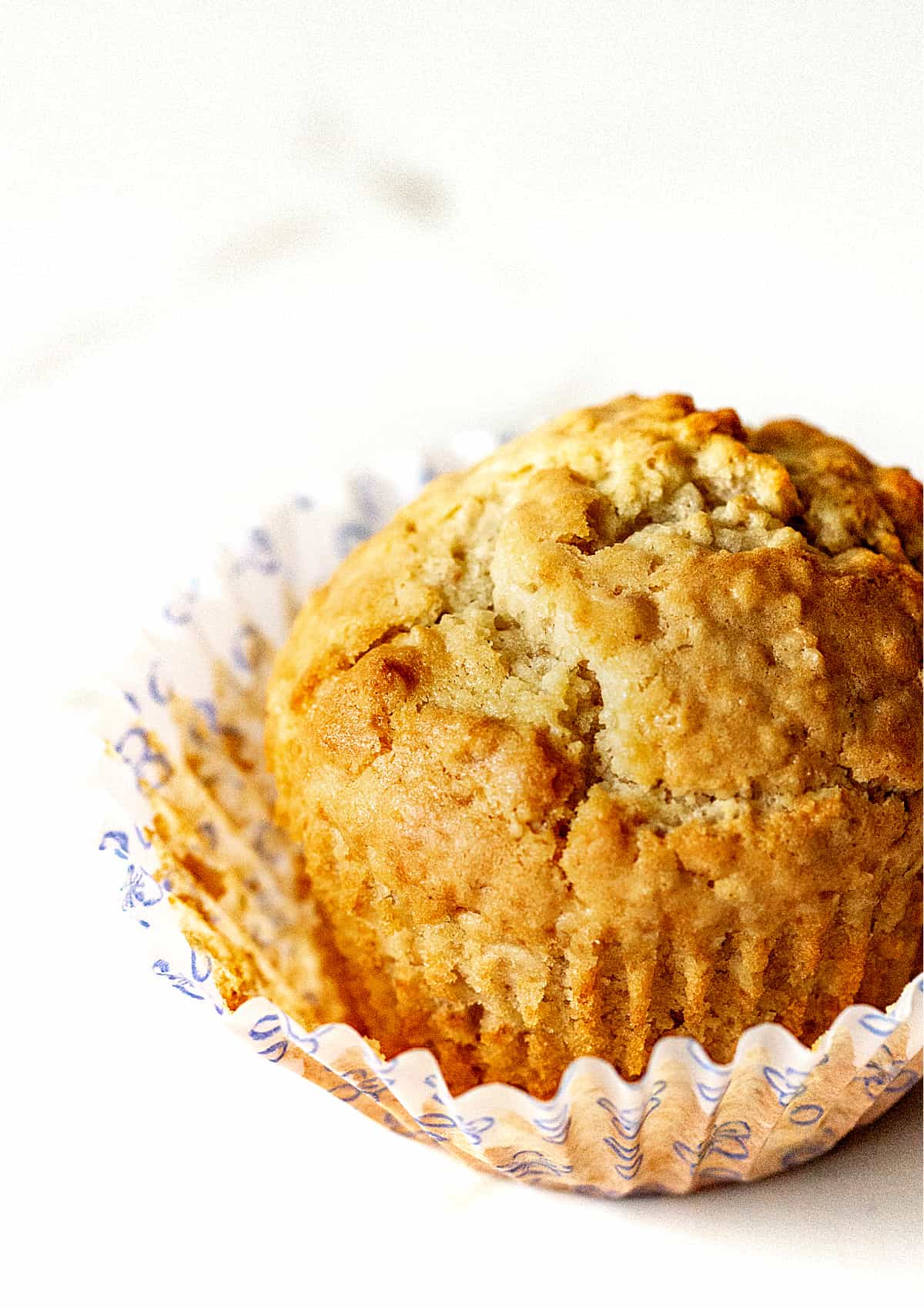 Single golden muffin on a white surface, opened paper cup