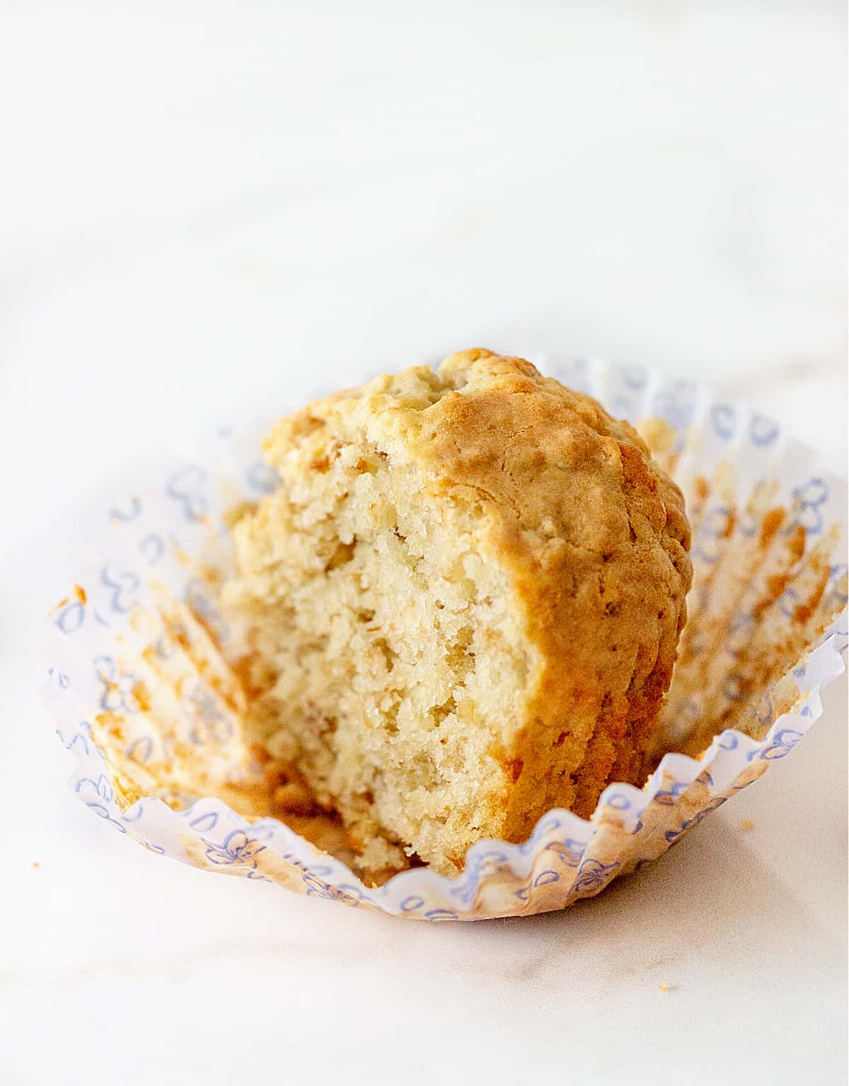 Half oatmeal muffin in light colored paper cup, white marble surface